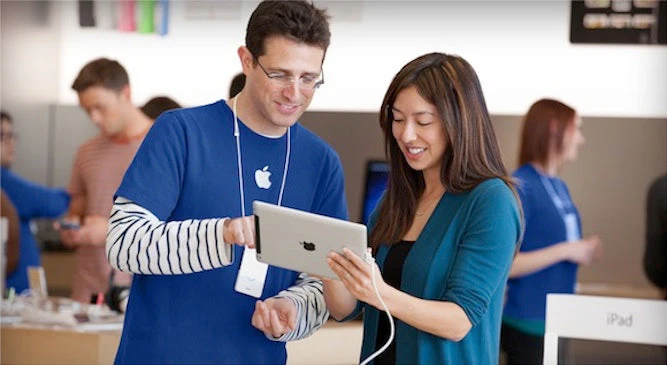 An image showing an Apple store employee giving a demo to a customer showing how using an iPad feels like, including its features, and benefits to understand and meet the customer's needs. 