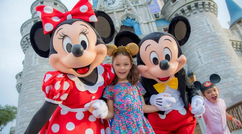 An image showing Mickey Mouse and Minnie Mouse holding hands with two happy and cheerful kids, posing together at Disneyland World Park.