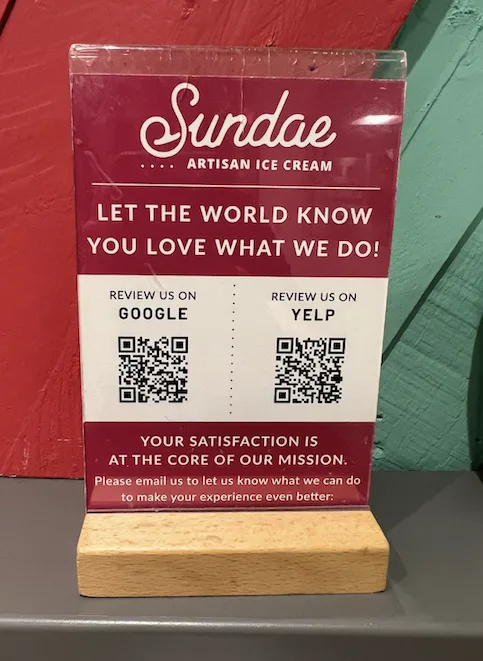 An image showing a review us card on the local ice cream shop where they have added a QR code to gather Google reviews and on Yelp. 